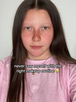 A young person with fair skin and dark brown hair is positioned in front of a plain white background, dressed in a light pink t-shirt. The person has light eyebrows, a slightly flushed nose, and neutral facial expression. The text "never saw myself with the right makeup routine" is overlaid at the bottom of the image in a white font.