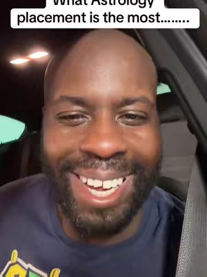 A close-up shot of a Black man smiling widely, revealing his teeth in a well-lit interior setting, likely in a car. The man has a bald head and a neatly trimmed beard. Text in a white font is overlayed at the top, and a car interior is slightly visible in the background.
