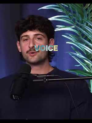 A man with a dark curly hairstyle and a mustache sits in front of a microphone. The word 'VOICE' is overlaid, and a plant is subtly visible at the right. He wears a dark shirt, and the background is blurred with a blue tint.
