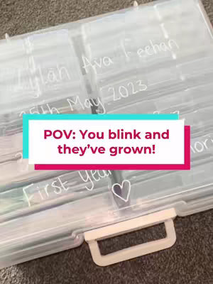 The image shows a clear plastic storage box, filled with organized compartments. Several sections are labeled with white handwritten text, including names and dates. A text overlay in a colorful frame is positioned centrally, with the text 'POV: You blink and they've grown!' In the lower right corner, a small heart symbol adds a touch of sentimentality to the image.