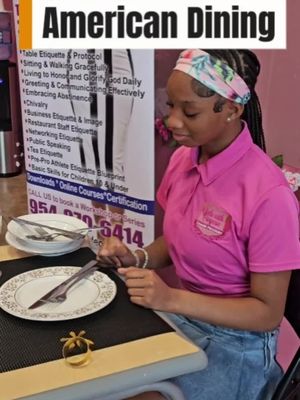 A young woman in a pink polo shirt and a floral headband is sitting at a table setting, with a white plate, utensils, and a gold napkin ring.