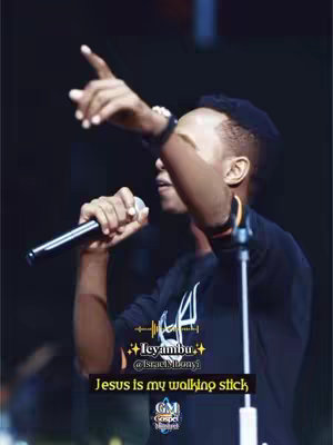 The cover image shows a man holding a microphone and singing on stage with his right arm pointing upwards, possibly during a live performance. The lighting appears dim, which is typical of stage setups, emphasizing the person in focus. Text overlays at the bottom include the title of the video with the performer's name, social media handle, and a religious quote.