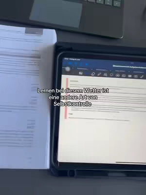 The image shows a workspace with a laptop, open notebook, and an iPad displaying text. The lighting is natural, highlighting the items on a dark surface.