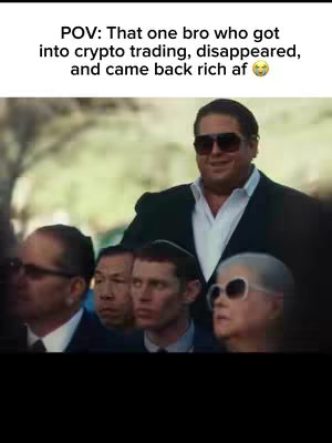 A man wearing sunglasses and a suit stands prominently in the foreground. Group of people with focused expressions are in the background.