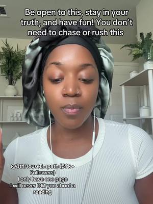 A woman with brown skin wears a black shower cap and a white top, gazing towards the camera. Text overlays are at the top, with additional text near the bottom of the frame. The background shows a simple, well-lit room with plants on shelves.
