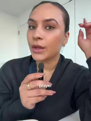 A woman with light skin and brown hair is the focus of a selfie-style shot. She is holding a small black microphone near her mouth. The background is blurred, suggesting an interior setting. The text overlay at the bottom reads 'prayer'.