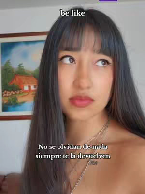 A young woman with long dark hair and bangs looks off to the side with a thoughtful expression. She is wearing a necklace. Text overlays such as: "be like" and a Spanish phrase are visible on the frame, partially visible within the frame as well.
