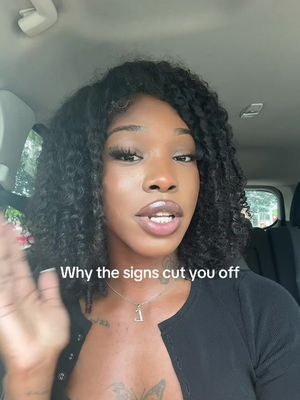 A woman with dark curly hair and a black top is seated inside a car. Text overlayed on the image reads, 'Why the signs cut you off.' She is looking at the camera . The background suggests a car's interior and surrounding environment.