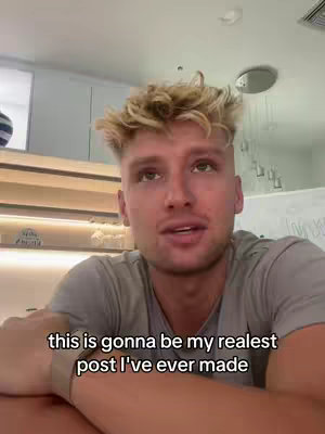 A man with short, highlighted, blonde hair looks upwards. The scene is indoors, with a pale-colored background and overhead lighting.