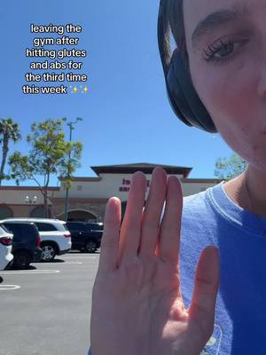 The cover image shows a selfie with a woman's hand in the foreground and her face partly visible. The background includes a parking lot, a building with a sign that reads 'to en', and a clear blue sky. The hand is in focus, with fingers spread, and the woman's eye peering over the top of it. The lighting appears to be bright and sunny.