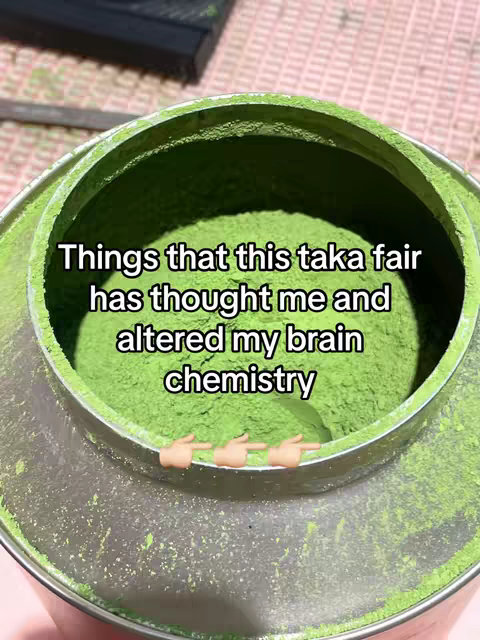 The image is an overhead shot of a metal container filled with bright green matcha powder. The container is slightly open, revealing the vibrant green contents. Text overlay and hand-pointing emojis are added.