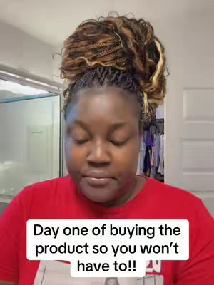 A woman with braided hair in a bun and a red shirt is shown looking down with a serious expression. Text is overlaid onto the image, in a white rectangle and black font, stating 'Day one of buying the product so you won't have to!!'. The background suggests a domestic setting.
