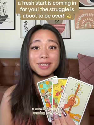 A woman is holding up three tarot cards while looking directly at the camera. The background includes a decorated wall and a framed picture. Text overlays are present at the top and bottom of the image, and they include messages about new beginnings and overcoming struggles.