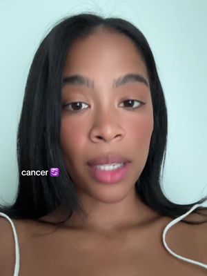 A close-up shot of a young woman with dark hair and fair skin. She's looking directly at the camera with a neutral expression, and light skin, against a light blue background. Overlayed on the image is a text box with the word "cancer" and the cancer zodiac symbol.