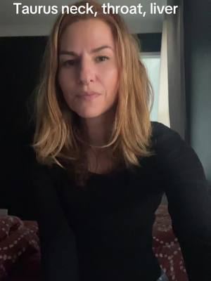The cover image features a woman facing the camera. She has shoulder-length blonde hair and is wearing a black long-sleeved shirt. The background is dark, with a glimpse of a window or curtain to the right. The text overlay at the top of the image says, 'Taurus neck, throat, liver'.
