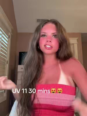 A young woman with long brown hair and a light complexion is the central figure, slightly off-center, smiling engagingly. She's wearing a red and white striped top. The background appears to be a room with neutral-toned walls and a partially visible window, creating a sense of a casual, indoor setting. Text overlays at the bottom indicates the timing for sun tanning