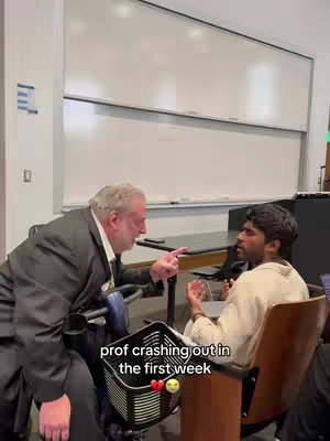 The image shows a professor, seated in what appears to be a mobility scooter, pointing aggressively at a student in a classroom setting. The student is sitting in a wooden chair, listening intently. The text overlay indicates a humorous situation related to college life.