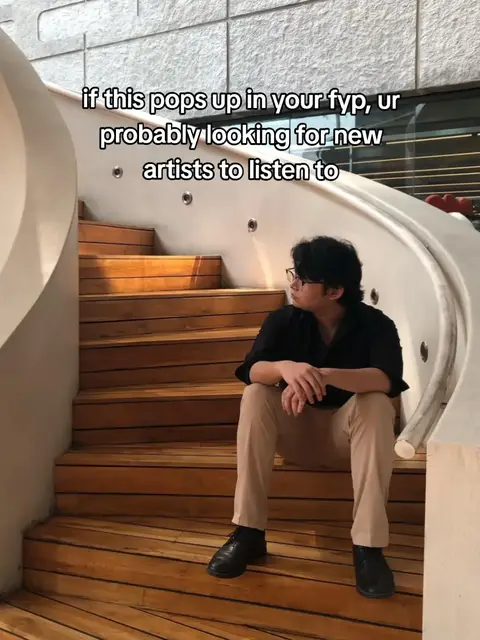 The cover image shows a young man sitting on a wooden staircase. He is wearing glasses, a black shirt, and tan pants, with a neutral expression. The background has an architectural touch, with some visible text overlayed on the image.