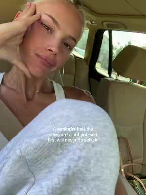 A selfie taken of a person sitting in a car seat. The person's face is in the foreground, with the interior of the car visible in the background. The person is fair-skinned with blonde hair, and is touching their face. Text is overlaid on the image with an inspirational message.