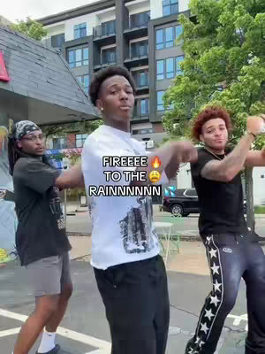 Three young men are dancing in front of a building with graffiti, a restaurant and trees in the background. Text overlay on the image.