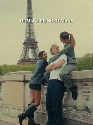 The cover image shows three young adults posing in front of the Eiffel Tower. The Eiffel Tower dominates the background. A pier is below the group. A young woman is in the foreground on the left, her back to the pier, with her arms leaning against the pier. She is wearing black clothes. In the middle a young man is being held up by another young woman. The group appears to be laughing and enjoy themselves.
