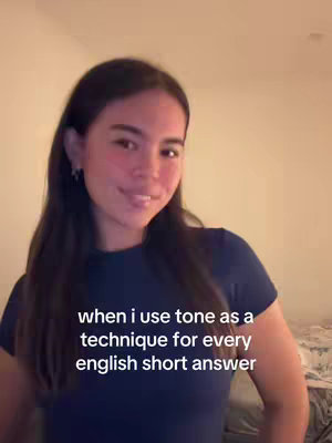 A young woman with long dark hair and dressed in a blue top is smiling, the text overlaid says: "when i use tone as a technique for every english short answer". The background is a simple, softly lit room.