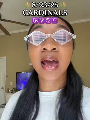 A selfie-style shot. The person, who appears to be a woman, is in the center of the frame, with a bright, open-mouthed expression. She is wearing clear, oversized diamond-shaped glasses. Above her head is text, also a selection of different signs. The background appears to be a light-colored wall with a ceiling fan visible at the top.
