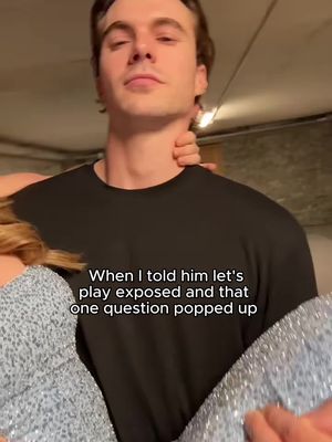 A man is being held by someone, likely a woman, with his head tilted slightly upwards. He has short, dark hair and is wearing a black t-shirt. The woman's arm is around his neck. Text overlayed on the image reads, "When I told him let's play exposed and that one question popped up."