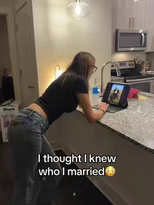 A woman is leaning on a kitchen counter, looking at a laptop displaying a picture. The kitchen has light cabinets, a stainless steel sink, and a clear pendant lamp. Text overlay appears in the image, at the bottom, with a background