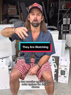 A man with long hair and a beard is sitting in front of boxes and equipment, with the text overlayed on a colored box.