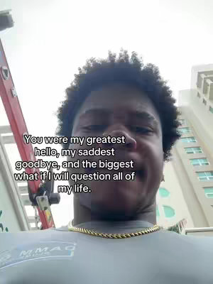 The cover image features a young man with a curly afro, positioned in a selfie style. The background is a blurred outdoor setting with what appears to be a building on the right and some construction equipment on the left. The man is wearing a grey t-shirt and a gold chain. White text is overlaid on the image.