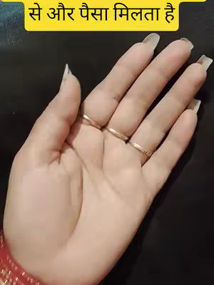 The cover image shows a person's hand. The hand is in the center of the image, and it is well-lit, with a neutral tone reflecting even lighting. The fingers are long and have clear, polished nails. The person is wearing rings on four of their fingers. In the upper part of the frame, a yellow rectangle encases text written in the Hindi language. The hand rests against a dark surface which could be a table or part of the person’s clothing.
