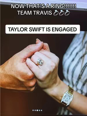 The image showcases two hands clasped together, with one prominently displaying a large diamond engagement ring. Above, white text on a black background reads, 'NOW THAT'S A RING!!!!!! TEAM TRAVIS' with ring emojis. Below, another white text banner states, 'TAYLOR SWIFT IS ENGAGED'. The background is dark, drawing focus to the hands and the ring.