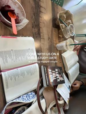 An overhead shot of a wooden table with various items related to bible study and a light meal. Two open Bibles, a book titled “Never Fall Again,” along with a purse and Starbucks items are arranged on the table. A small bowl of what appears to be acai and a spoon are visible, indicating a snack or meal alongside the bible study. Text overlayed on the image reads, “COME WITH US ON A BIBLE STUDY DATE as a young engaged couple.”