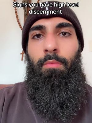 A close-up shot of a man's face. He has a dark beard and a black beanie. The text overlay at the top says, "Signs you have high level discernment."
