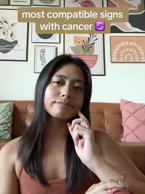 The image shows a woman looking at the camera, with a light brown background. There is a text overlay at the top that reads "most compatible signs with cancer". The woman has long dark hair, and is wearing a light orange top.