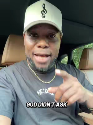 A man in a car talks to the camera, wearing a hat with a musical note and a necklace, with text overlayed.
