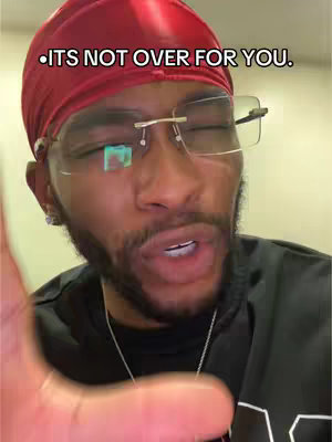 A close-up shot of a man wearing a red durag and glasses. He is looking directly at the camera with a serious expression, and his mouth is open as if speaking. Text overlayed on the image reads, 'ITS NOT OVER FOR YOU.' The overall composition focuses on the man's face.
