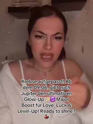 The image is a selfie-style video cover featuring a woman with dark hair and makeup, set against a blurred background. Text overlays are centrally positioned, offering astrological insights. The woman's expression is focused, suggesting direct communication to the viewer.