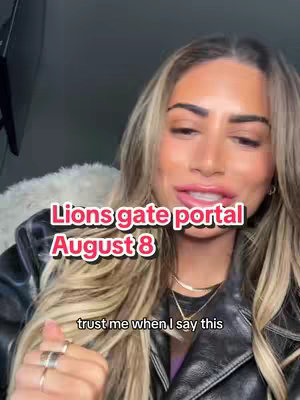 A woman with long blonde hair and makeup is looking at the camera and speaking. Overlayed text in pink and white on a black background says 'Lions gate portal August 8'. The woman is wearing a black leather jacket and a white fluffy top.