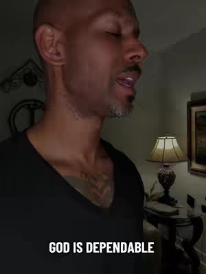 The cover image shows a close-up of a Black man singing. The man is bald, with a trimmed gray beard. He is wearing a black v-neck shirt. Behind him is a lamp and part of a framed picture on the wall. Text overlayed at the bottom says, 'GOD IS DEPENDABLE'.