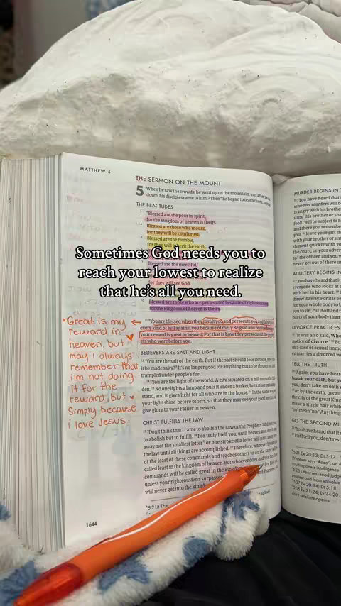 The image shows an open Bible on a bed. Colorful highlighting and handwritten annotations are visible on the pages. An orange pen rests on the pages.