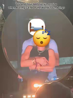 The cover image presents a scene at a concert, enveloped within a clear circular shape. Within this circle, a person is embraced from behind. The head of the person being embraced has been replaced with a yellow emoji with closed eyes. Overlaid on these figures is an emblem of a brown bed with blue bedding, and a series of 'Z's suggesting sleep. The background portrays a blurred concert setting, with dim lighting and the suggestion of a stage. Above the figures, there is text in a sans-serif font.