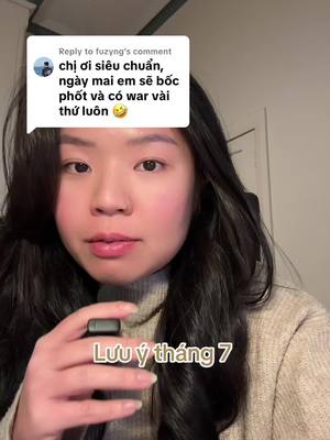 A woman with long dark hair is in a selfie-style video. She is holding a small device near her mouth. Overlayed text in Vietnamese is present at the bottom of the frame. A comment bubble with text in Vietnamese covers the top left. The woman's face is in focus against a neutral background.