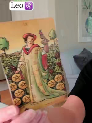 The cover image shows a tarot card held in a person's hands. The card depicts a woman in a long, flowing cream-colored robe holding nine golden coins. The card is held in front of a background that is partially visible and shows a home setting with floral elements and a framed image, likely a painting or photograph, hanging on the wall. The words 'Leo' can be seen above the tarot card.