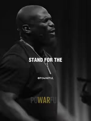 A monochrome close-up shot features a Black man in profile, speaking into a microphone. Text overlayed on the image reads "STAND FOR THE" in bold, centered white text. Below this, the handle "@POWARFUL" is in smaller white text. The background is blurred, suggesting a stage or event setting.