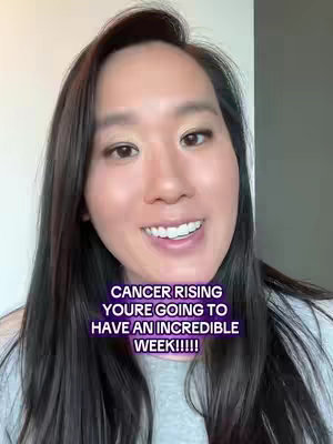 A selfie-style video cover featuring a light-skinned woman with long dark hair. She is centered in the frame, looking directly at the camera with a friendly smile. The background is simple, with a neutral-toned wall visible. Overlayed text in a purple-to-pink gradient box reads, "CANCER RISING YOU'RE GOING TO HAVE AN INCREDIBLE WEEK!!!!"
