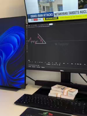 The image shows a desk with three computer monitors. One monitor displays a stock chart with a triangular pattern, another shows news about Israel-Iran attacks, and the third has a blue and white abstract design. There are stacks of money, a keyboard, and a mousepad on the table. The overall theme suggests a focus on finance, trading, or investments.