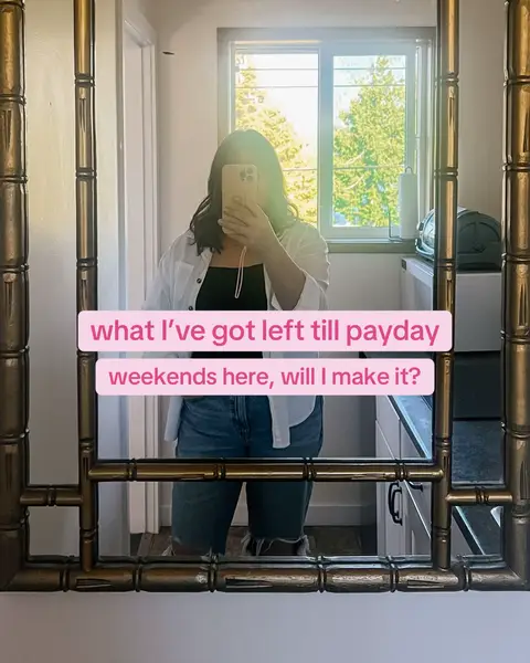A person is taking a mirror selfie in a golden bamboo-framed mirror. The person is holding their phone up, obscuring their face. They're wearing a white button-down shirt over a black top and denim shorts. Text overlayed on the image reads, 'what I've got left till payday weekends here, will I make it?'