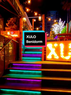 The cover image shows a bar in Benidorm at night with colored lights illuminating stairs and the bar's signage, displaying 'XULO' prominently. A text overlay displays the bar's name and location.